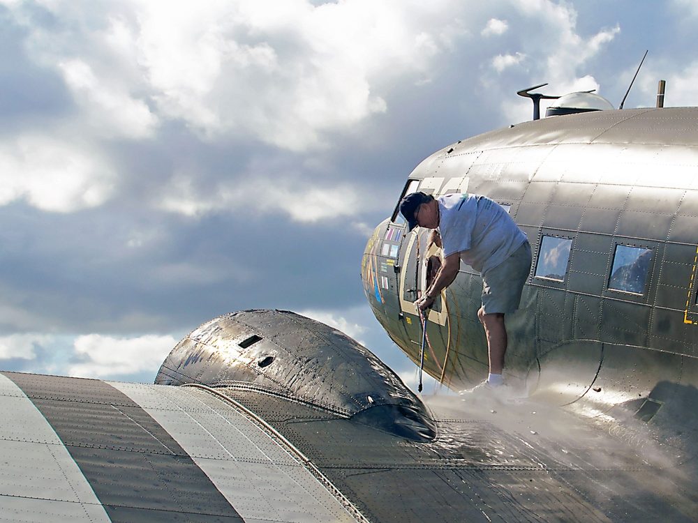 A worker washing the polished fuselage of a propeller aircraft