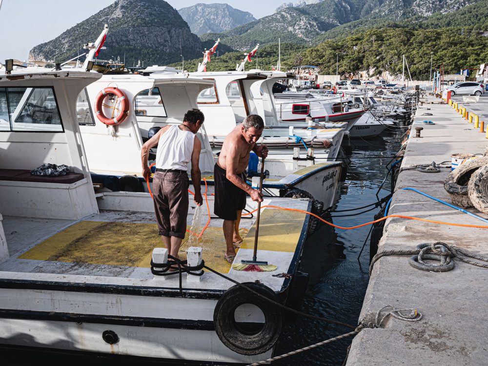 Two people washing down boats moored along a marina dock