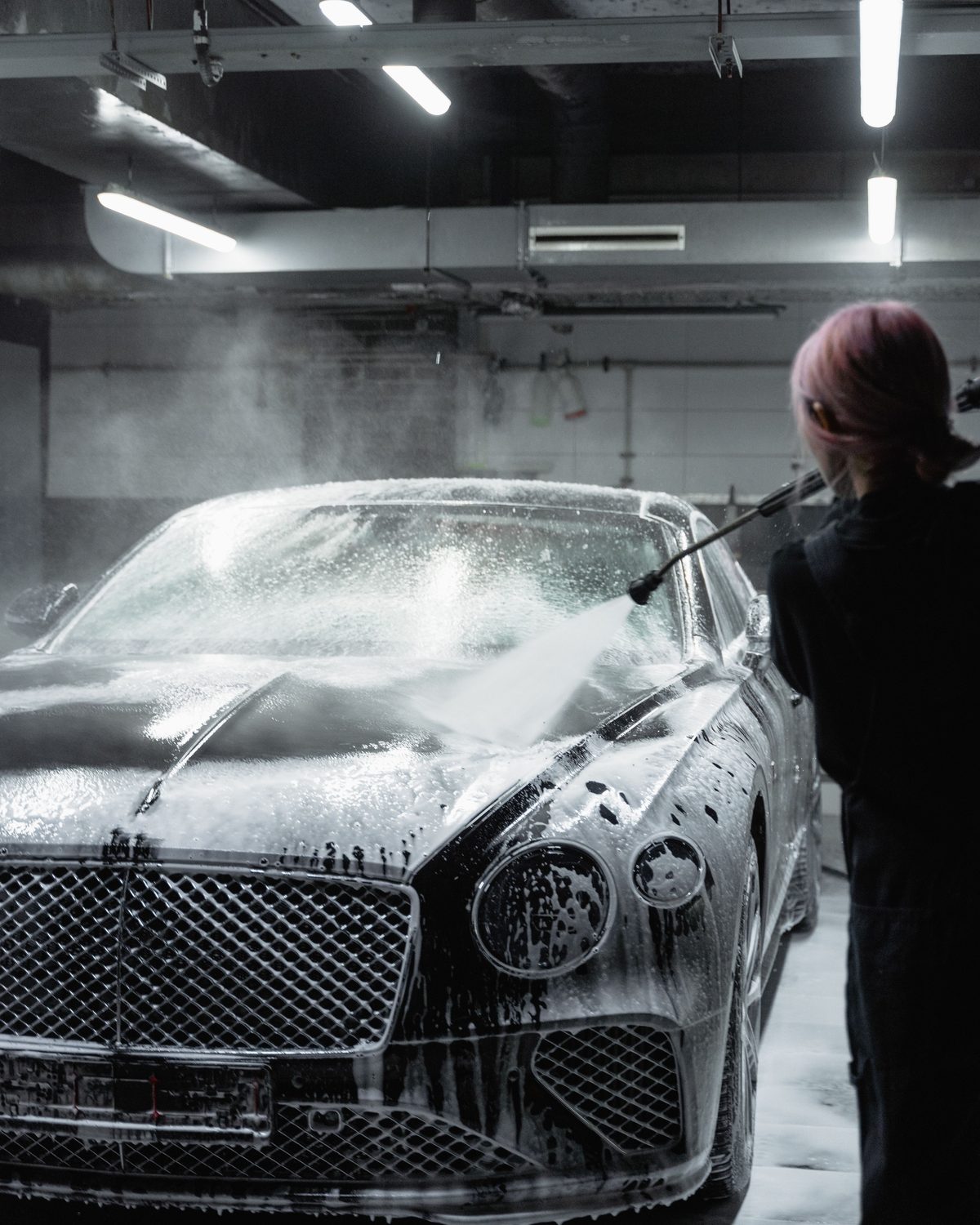 A detailer pressure-washing foam from a car in a dark garage